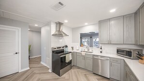 Una cocina moderna con gabinetes grises, una campana extractora de acero inoxidable, horno empotrado, lavavajillas y microondas.