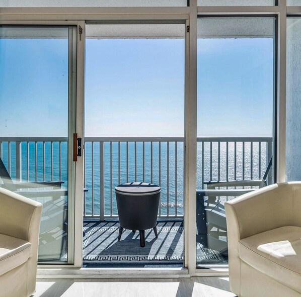 A balcony with a view of the sea, a round table, and two chairs.