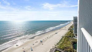 A beach view from a balcony overlooking a sandy beach with a clear sky. - A direct oceanfront king bedroom: balcony, pool, coffee bar, wash & dryer  (Myrtle Beach)