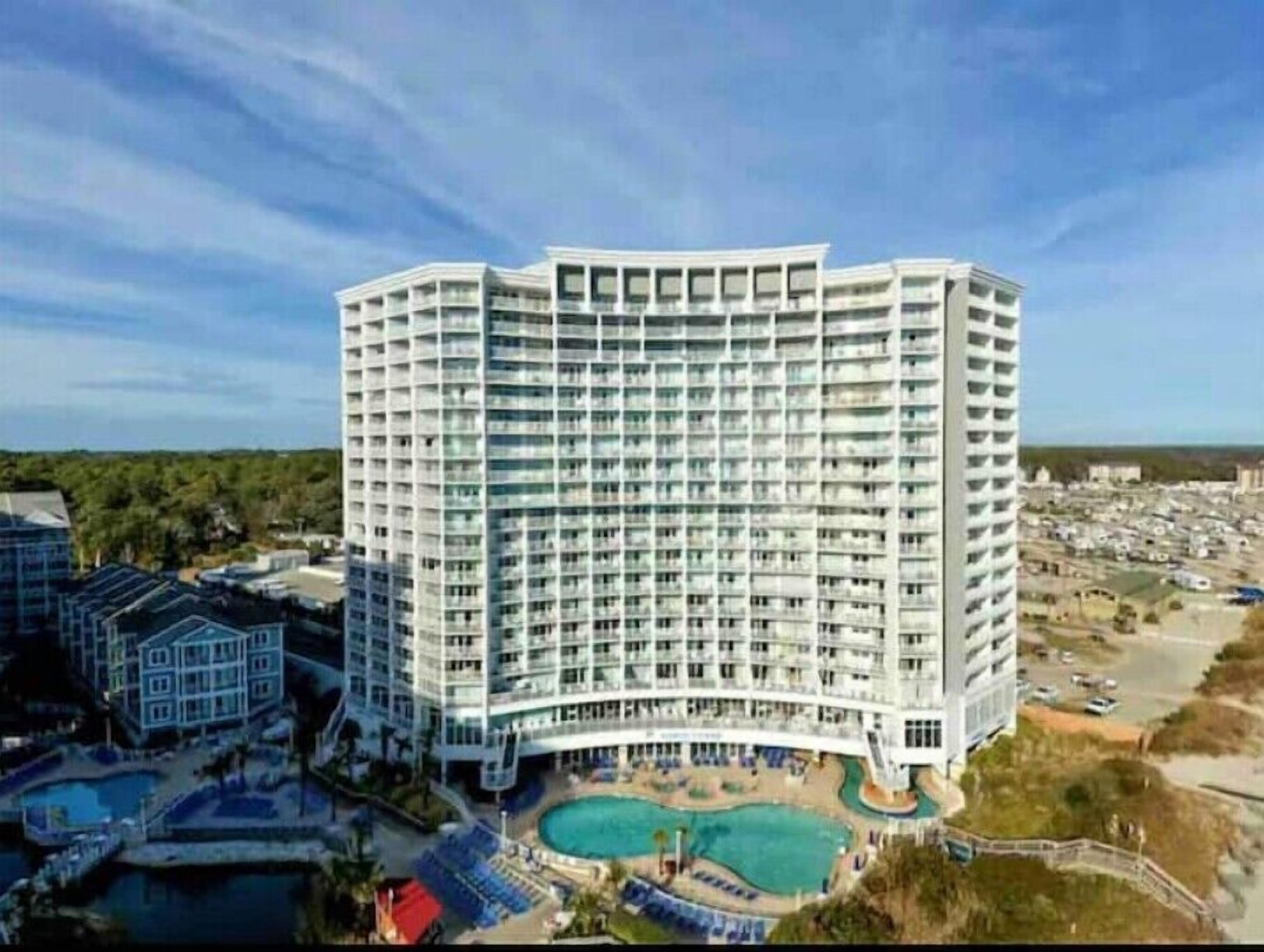 Un hôtel de grande hauteur doté de nombreux balcons, d’une cour intérieure avec une piscine et offrant une vue sur les environs.