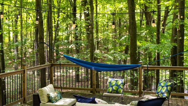 Eine Terrasse mit Korbmöbeln und einer Hängematte, umgeben von einem Wald.