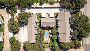 An aerial view of a residential area with multiple detached houses, a central swimming pool, and surrounding greenery.
