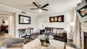 A living room with a ceiling fan, a sofa, a coffee table, and a fireplace. - I00 - Gated Irving 2BR | DFW 10Min | Patio + Pool (Irving)