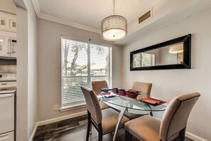 Uma sala de jantar com mesa de vidro, cadeiras e luminária pendente.