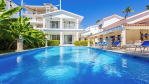 A swimming pool with lounge chairs and a two-story building with balconies. - Beachfront 8BR Villa with Pool & Maid (Punta Cana)
