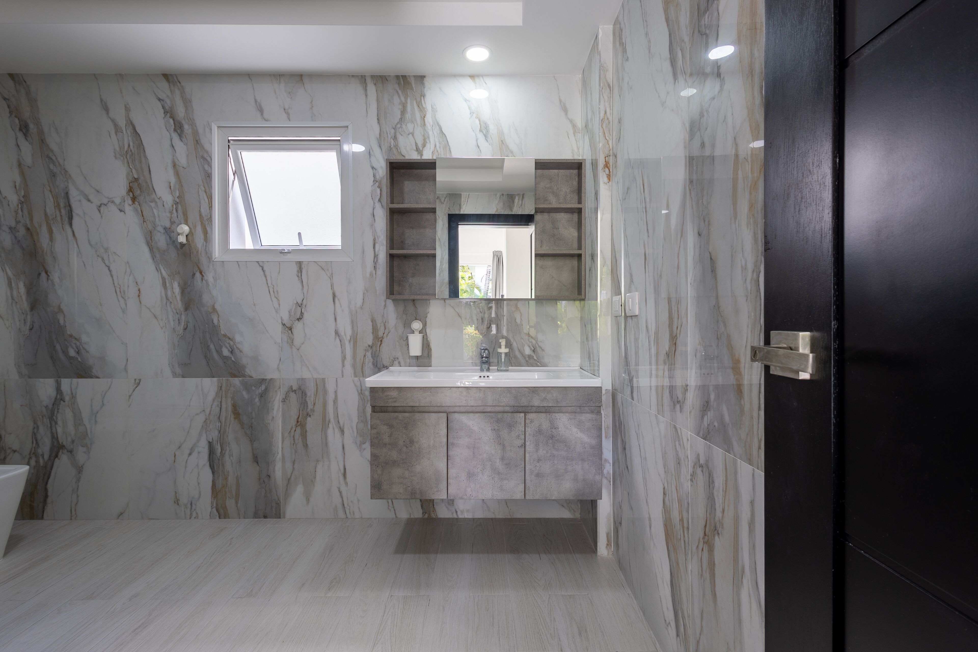 A bathroom with marble walls, a built-in sink, and a dark door.
