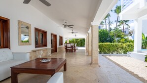 A spacious indoor area with a ceiling fan, a wooden coffee table, a white sofa, and a dining table with chairs. - Beachfront 8BR Villa with Pool & Maid (Punta Cana)