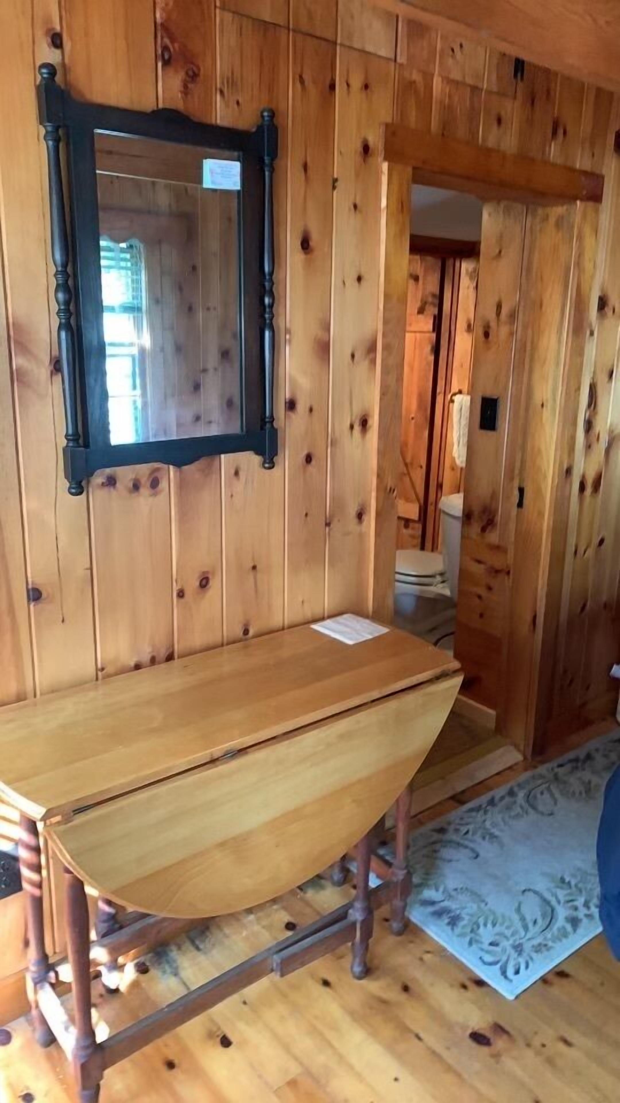 A wooden interior with a large mirror, a wooden table, and a patterned rug.