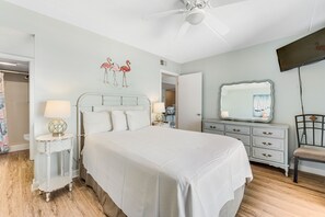 Une chambre à coucher comprenant un lit, des tables de chevet, un ventilateur de plafond, un miroir et un téléviseur.