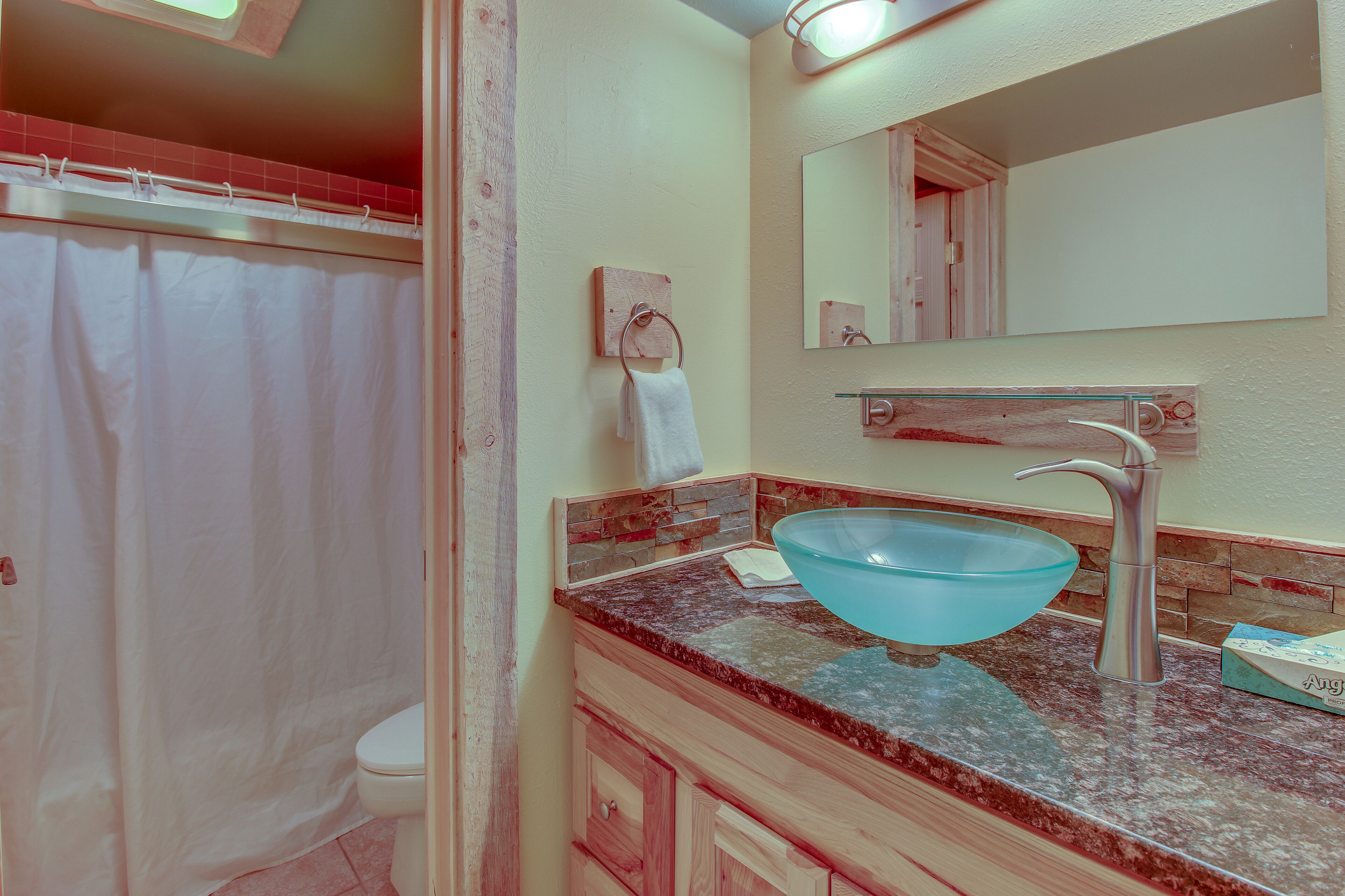 Une salle de bain avec un lavabo en forme de bol en verre, des toilettes blanches et un rideau de douche.