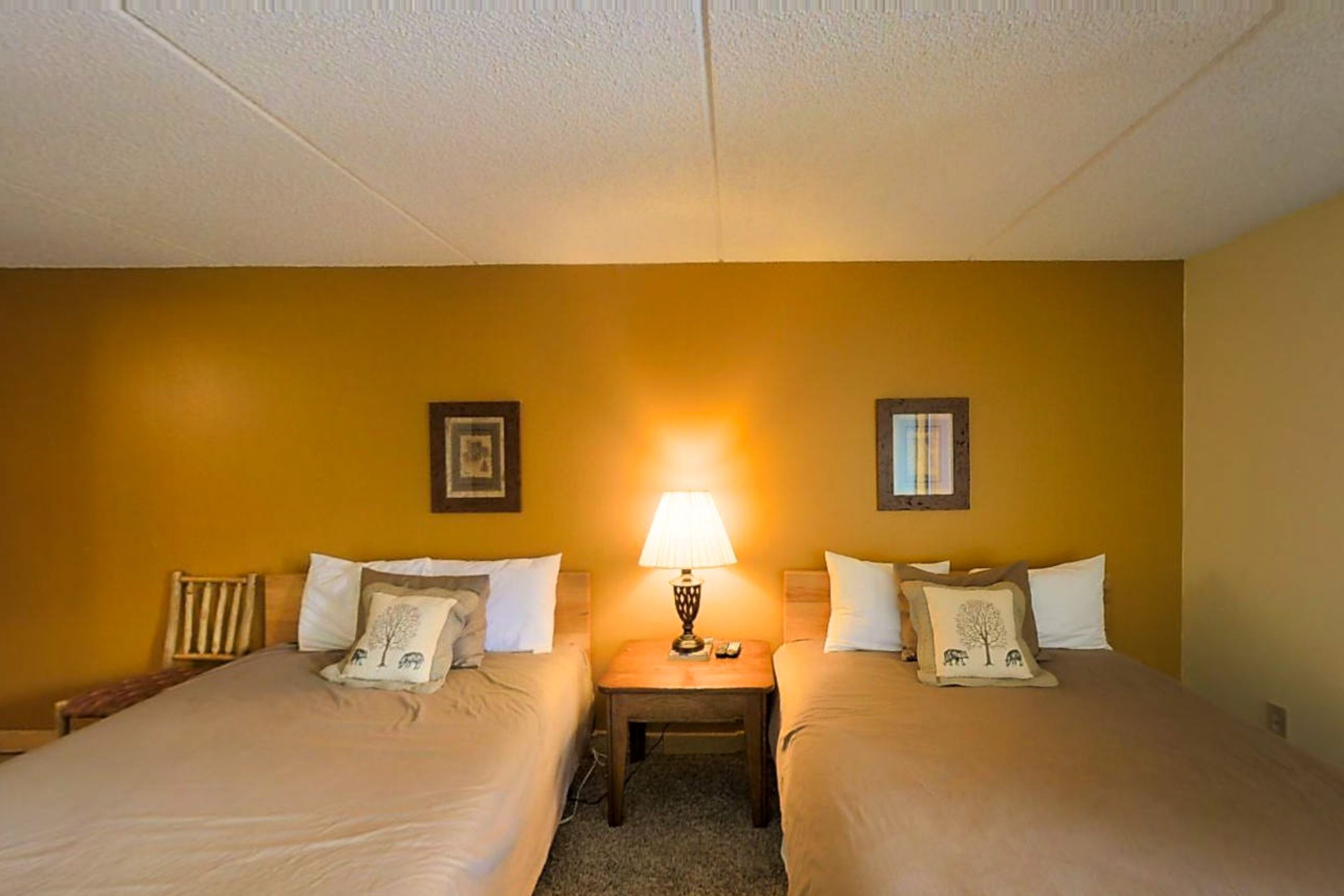A hotel room with two beds, a nightstand with a lamp, and a framed picture on the wall.