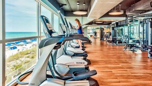 Une salle de sport équipée de machines de cardio et de matériel de musculation, avec de grandes fenêtres donnant sur la plage.