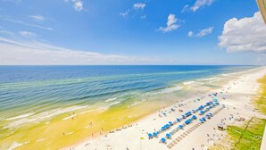 Une plage bordée d’une rangée de parasols bleus et de chaises longues, un rivage sablonneux et l’océan.