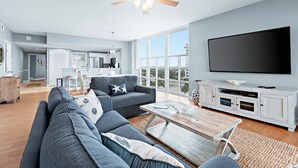 A modern living room with a grey sectional sofa, a wooden coffee table, and a large flat-screen TV on a white cabinet. - Sterling Shores (Destin)