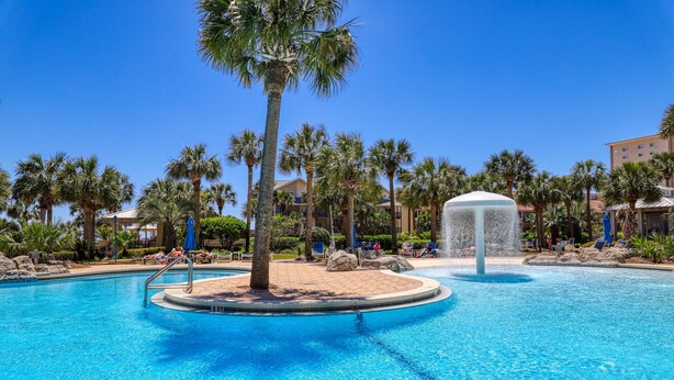 A swimming pool with palm trees, lounge chairs, and a water fountain. - Sterling Shores (Destin)