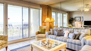 A spacious living room with a large sofa, a coffee table, and a balcony with outdoor seating. - Sterling Shores (Destin)