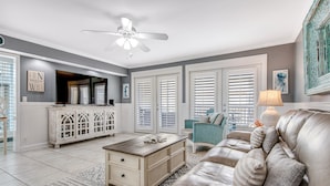 A living room with a white cabinet, a beige sofa, and a ceiling fan. - Sandpiper Cove (Destin)