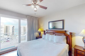 A hotel room with a large bed, a ceiling fan, a balcony with a view of the city, and a window with curtains. - Laketown Wharf (Panama City Beach)