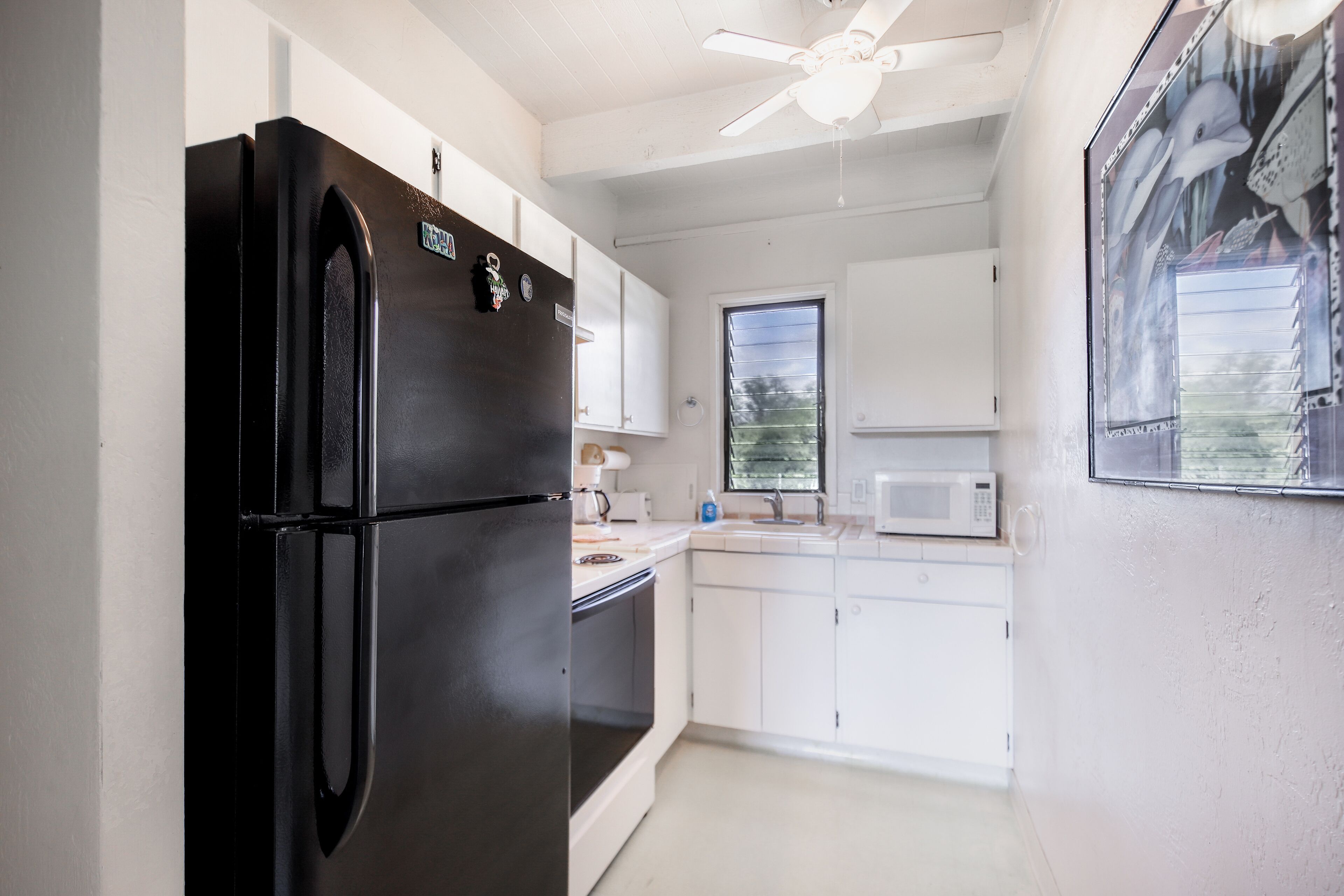 Una cocina con armarios blancos, un refrigerador negro, un microondas y un ventilador de techo.
