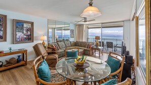 A spacious living room with a glass table, comfortable seating, and a view of the ocean.
