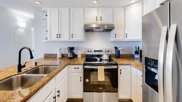 A modern kitchen with white cabinets, stainless steel appliances, granite countertops, and a double sink.