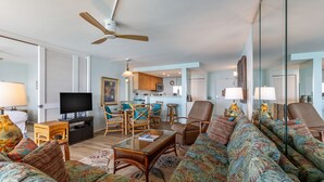 A spacious living room with a sofa, chairs, a coffee table, and a television. - Hololani Resort (Lahaina)