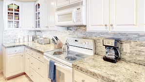A kitchen with white cabinets, a granite countertop, a stove, a microwave, and a coffee maker. - Hololani Resort (Lahaina)