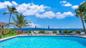 A clear blue pool with lounge chairs and umbrellas, surrounded by palm trees and a view of the ocean. - Vacasa at Hotel Molokai (Kaunakakai)