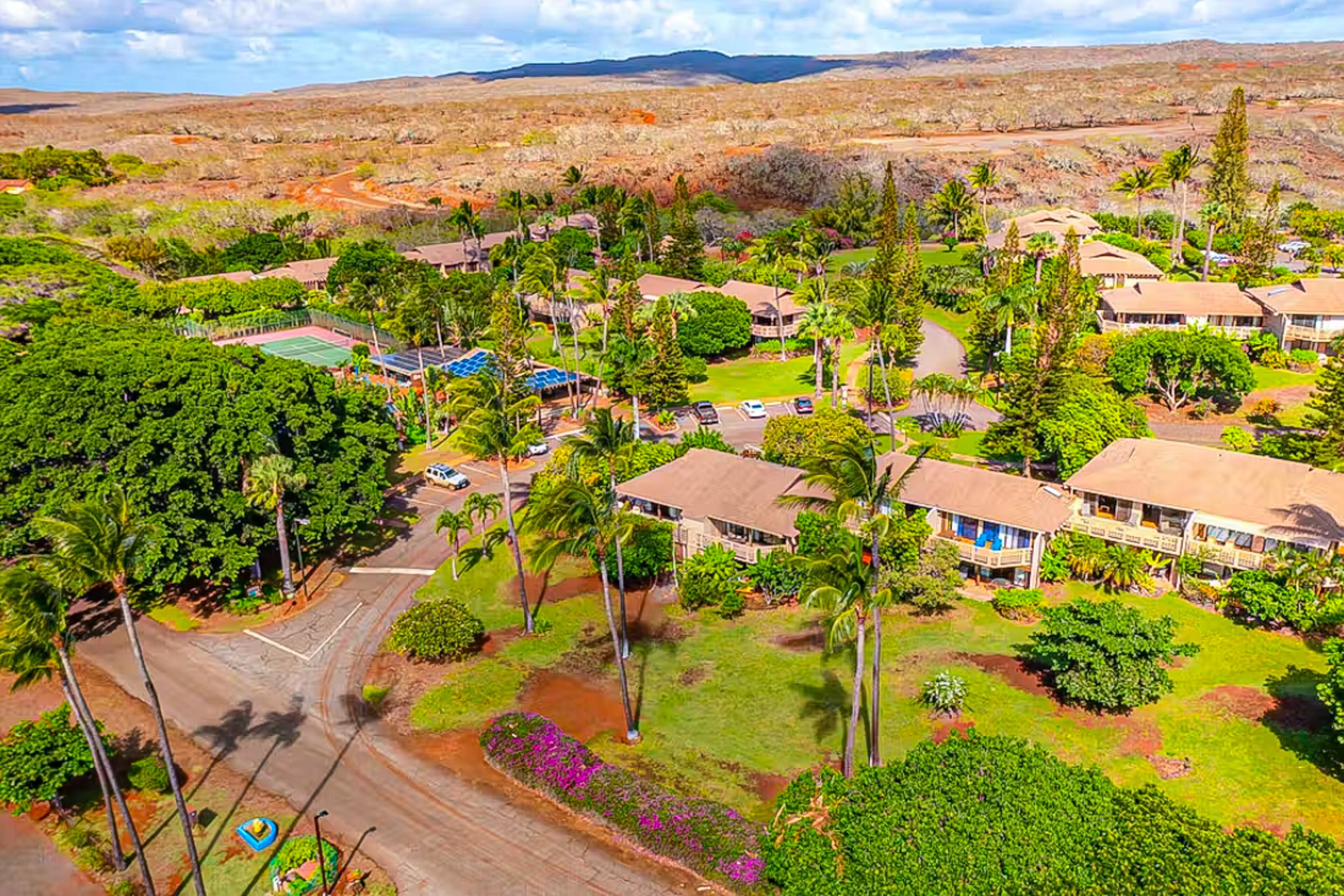 An aerial view of a resort with multiple bungalow-style buildings, a tennis court, and lush greenery.