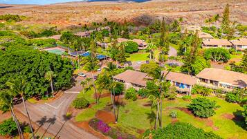 An aerial view of a resort with multiple bungalow-style buildings, a tennis court, and lush greenery.
