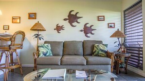A living room with a sofa, two side tables, a glass coffee table, and wall art. - Molokai Shores (Kaunakakai)