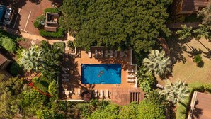 Luchtbeeld van een woonhuis met zwembad, omringd door weelderige begroeiing en palmbomen.