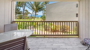 A balcony with a table and chairs, a view of a golf course, and a palm tree. - Wavecrest (Kaunakakai)