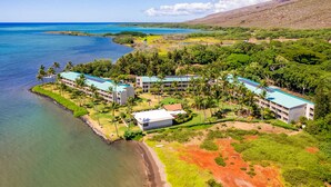An aerial view of a resort with multiple buildings, a beachfront, and surrounding greenery. - Wavecrest (Kaunakakai)