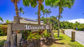 A wooden sign with the name 'Wavecrest Resort' surrounded by tropical plants and palm trees. - Wavecrest (Kaunakakai)