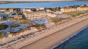 Vue aérienne d’un hôtel situé sur la côte, composé de plusieurs bâtiments, avec une plage de sable et une vue sur l’océan.