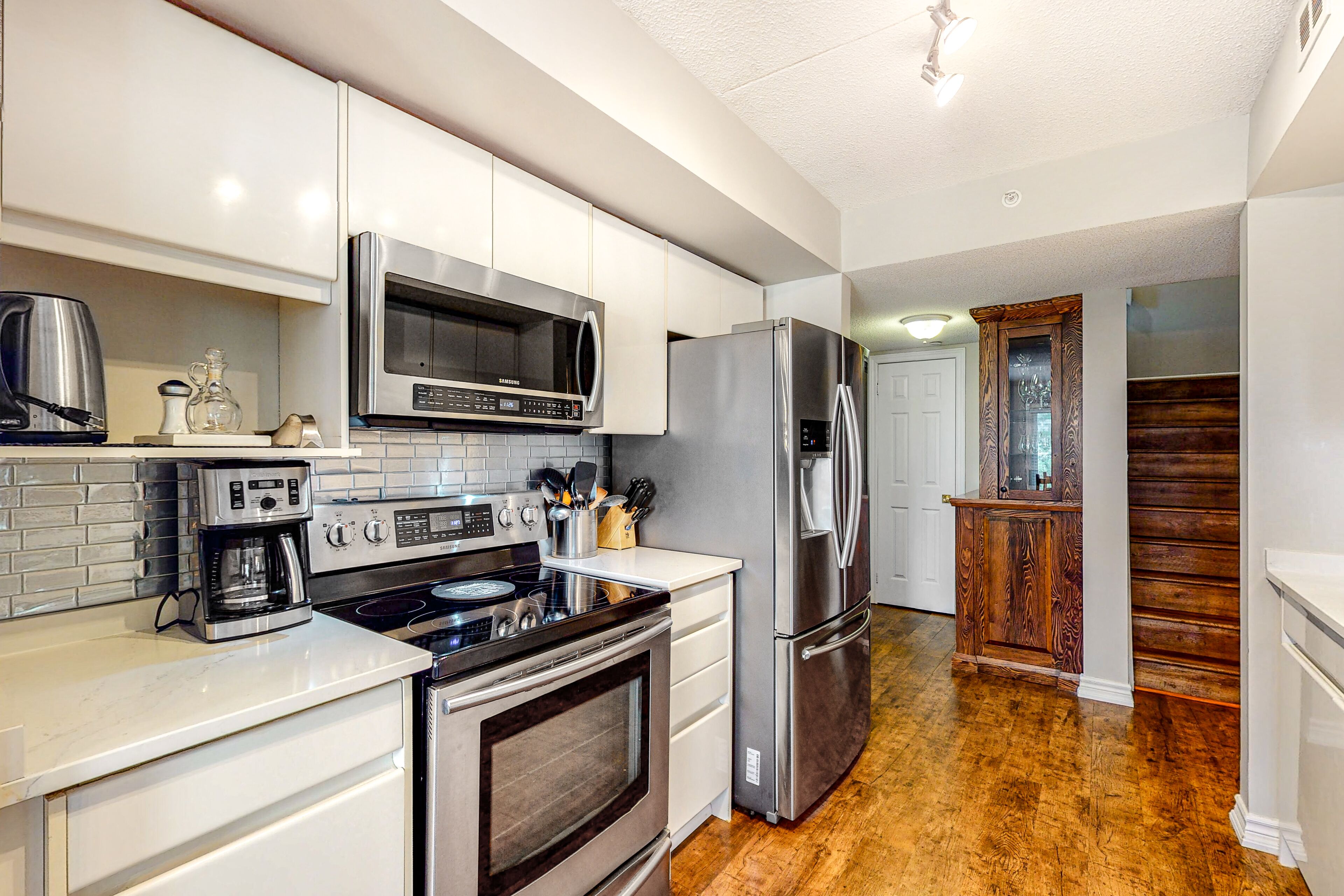 A modern kitchen with stainless steel appliances, white cabinetry, and a wooden floor.