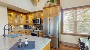 A modern kitchen with wooden cabinets, stainless steel appliances, a granite countertop, and a large window. - Snowbridge (The Blue Mountains)