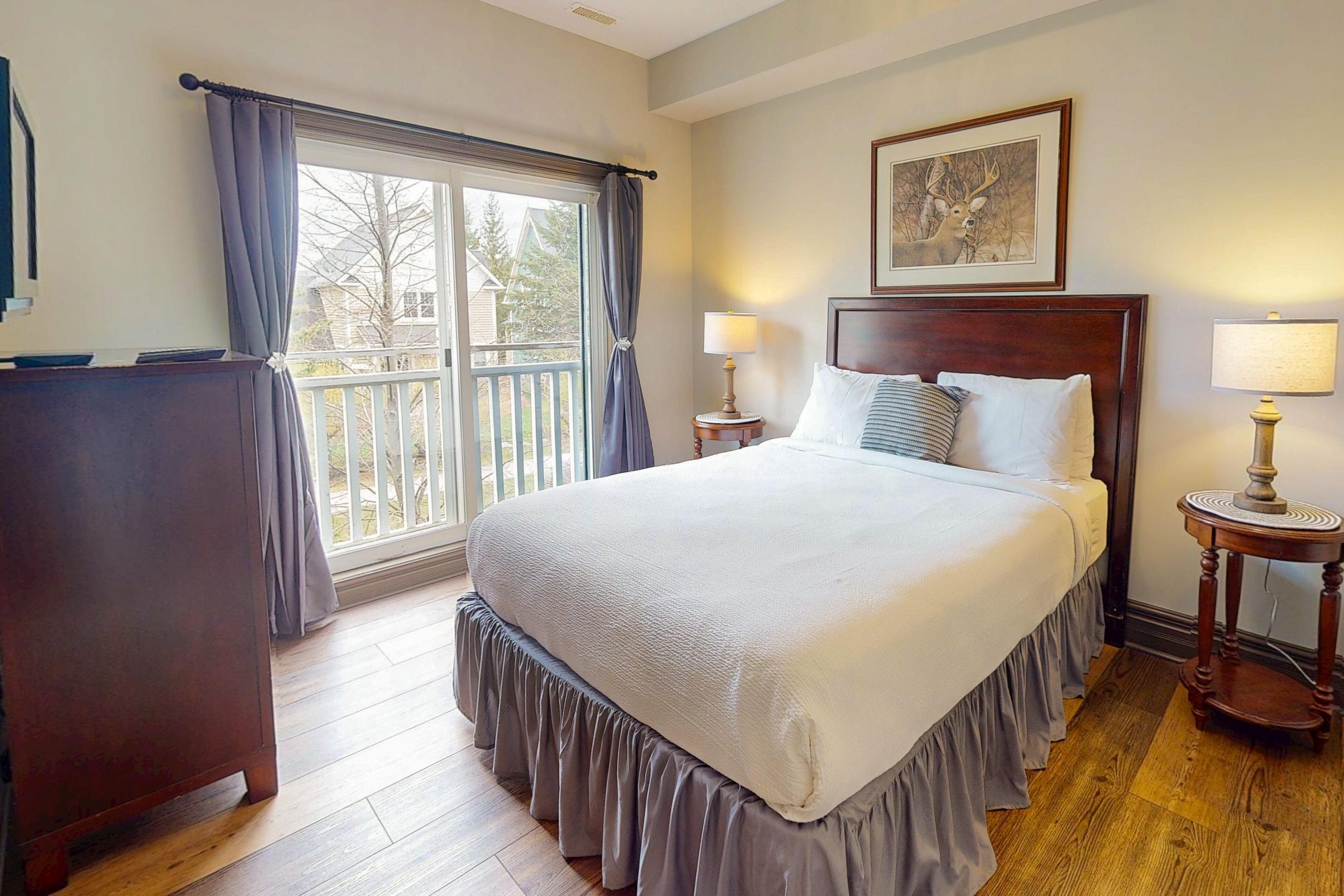Una habitación de hotel con una cama grande, dos lámparas de noche, un aparador de madera y una ventana con cortinas.
