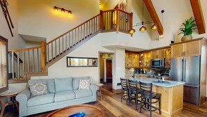 A spacious living area with a sofa, coffee table, and a kitchen with wooden cabinets and stainless steel appliances. - Snowbridge (The Blue Mountains)