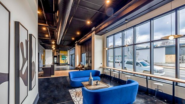 A modern interior with a blue sofa, a coffee table, and large windows offering a view of the street. - Muse Nashville (Nashville)
