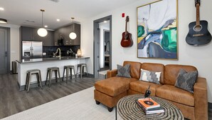 A modern living room with a brown leather sofa, a coffee table with books, and a kitchen area in the background. - Muse Nashville (Nashville)