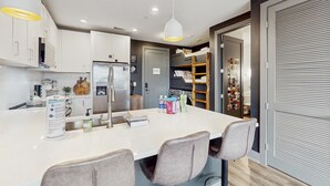 A modern kitchen with white cabinets, a central island with chairs, a refrigerator, and a sink. - Muse Nashville (Nashville)
