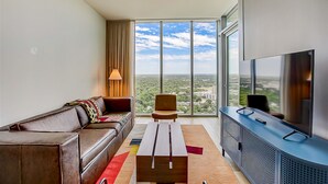 Een moderne woonkamer met een grote televisie, een bank, een fauteuil en een stadszicht door grote ramen.