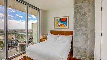 A hotel room with a large bed, a view of the city, and a balcony with chairs.