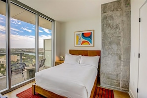 Une chambre d’hôtel avec un grand lit, une vue sur la ville et un balcon équipé de chaises.