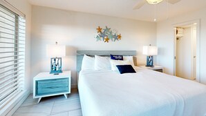 A bedroom with a bed, nightstands, a ceiling fan, and a wall decoration. - Suntide II Condominiums (South Padre Island)