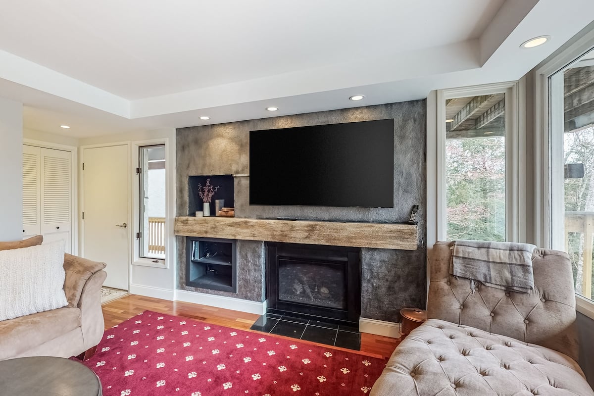A modern living room with a fireplace, a large flat-screen TV mounted above it, and a comfortable seating area with two sofas and a coffee table.