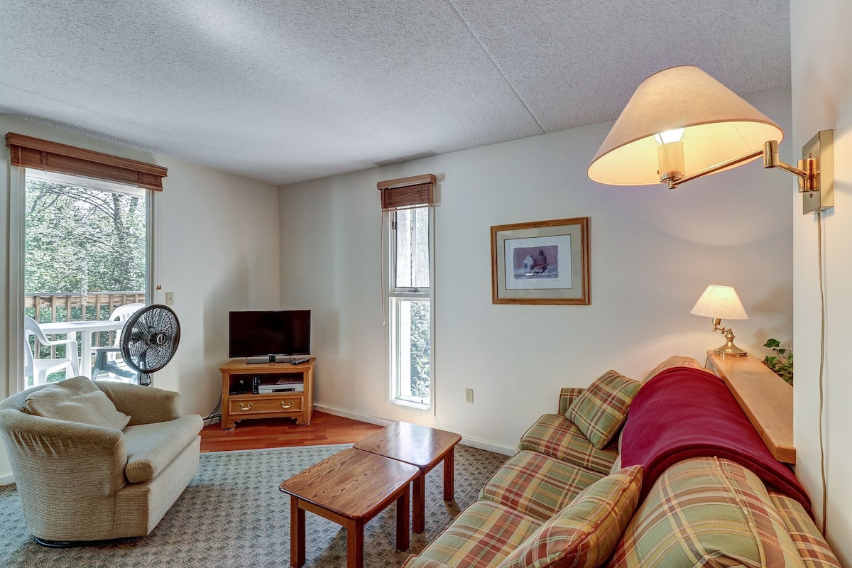 A living room with a sofa, a wooden coffee table, a television on a stand, and a fan.