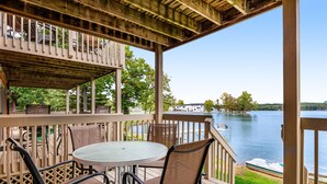A wooden deck with a round table and chairs, overlooking a lake with boats and a house in the background. - Thunderbird Resort Condo (Wisconsin Dells)